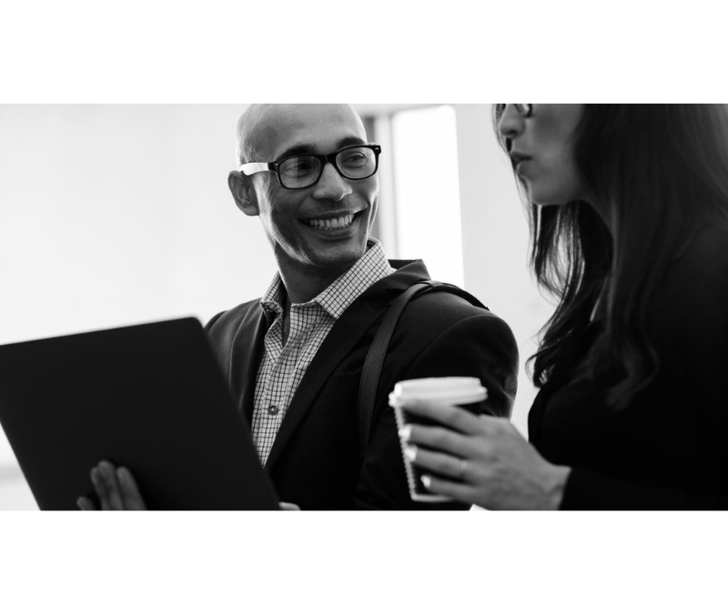 Smiling businessman holding laptop looking at female colleague in office