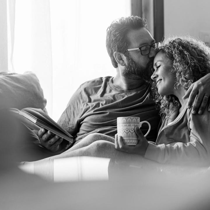 Male and female relax on the couch reading a book and drinking a tea