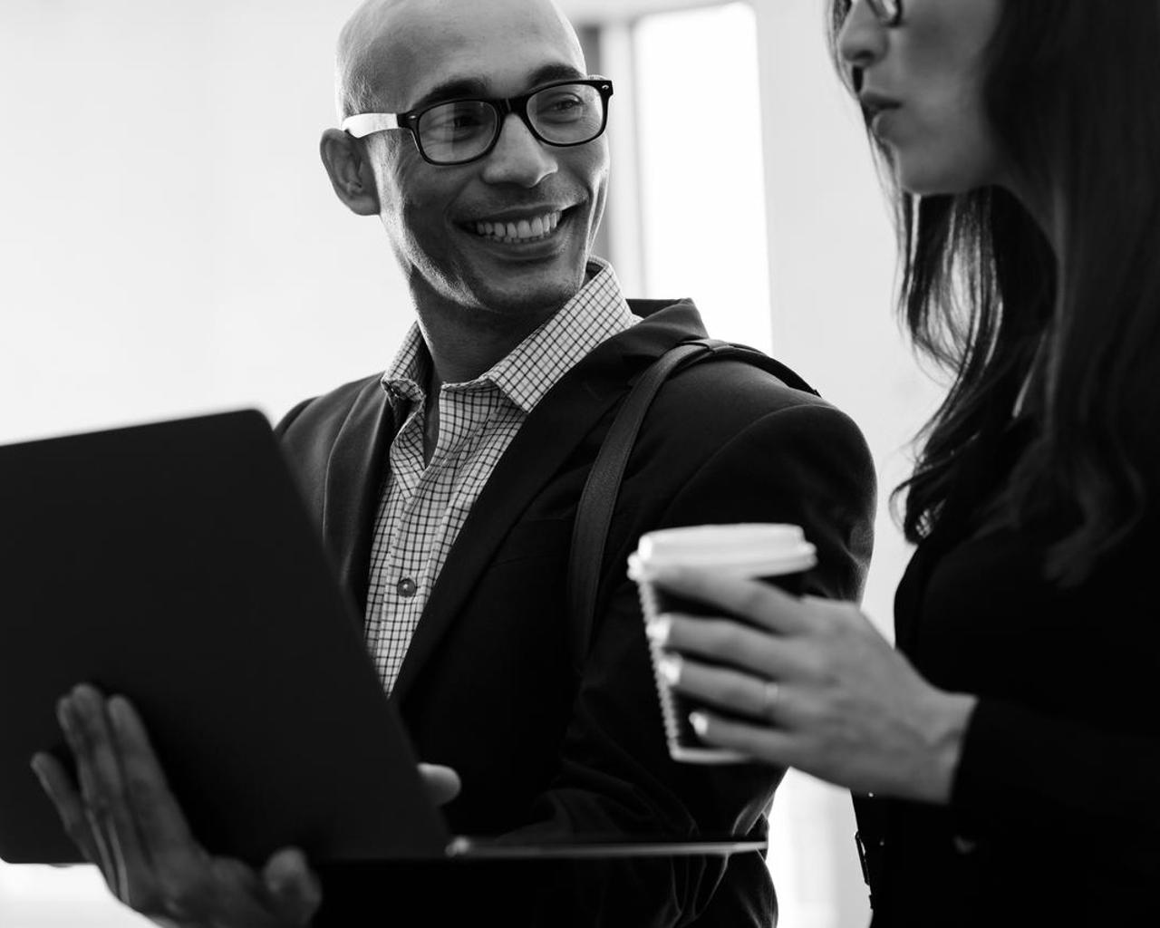 Smiling businessman holding laptop looking at female colleague in office