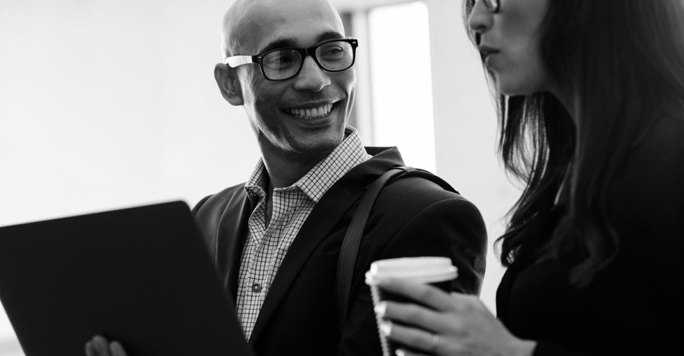 Smiling businessman holding laptop looking at female colleague in office