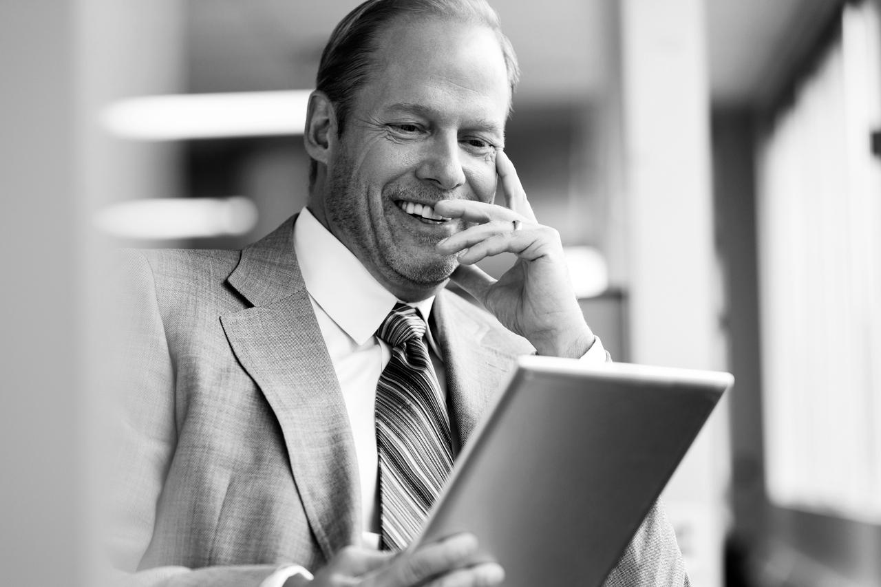 Middle-aged business man in office with tablet computer Middle-aged business man smiling and using tablet computer in office