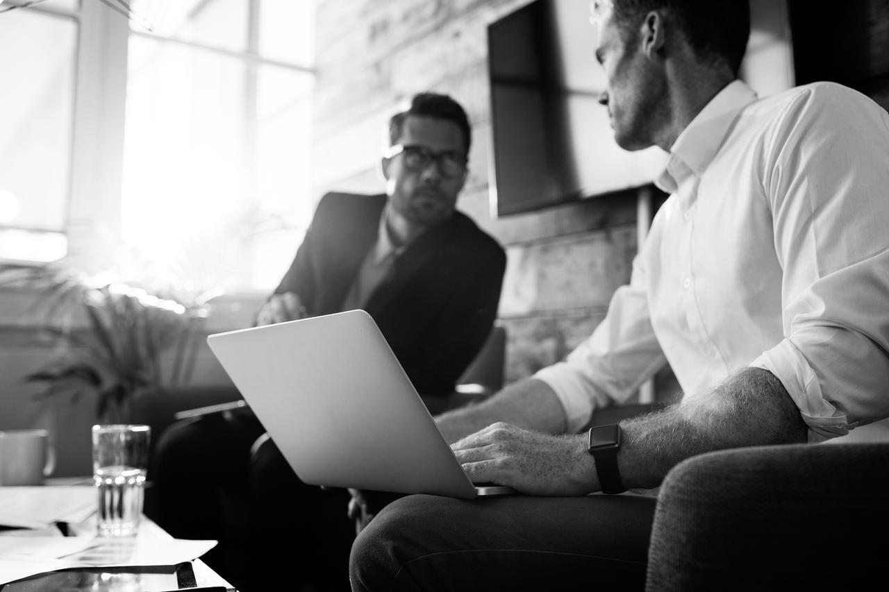 Businessman with laptop talking with colleague during meeting Two young men sitting in an office and discussing business with a laptop